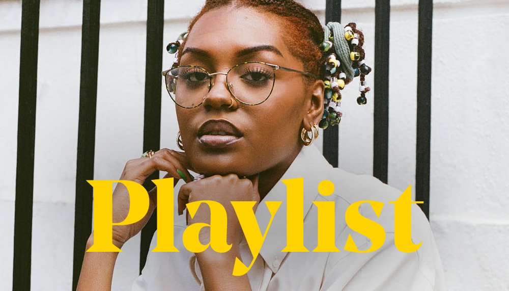 Singer Monét sits on concrete steps with black railings outside a white London building, she wears a white shirt and glasses. The word 'playlist' in yellow type overlays the image