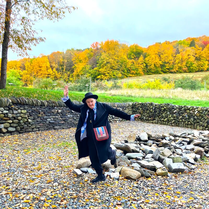 Poet CA Conrad steps on stones, with a field and trees in the background