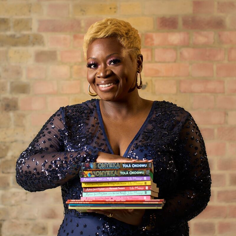 Author Tola Okogwu holding a stack of books and wearing a navy sequinned top and hoop earrings.