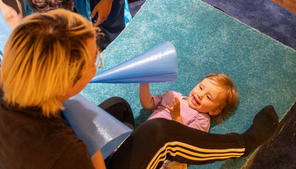 Parent sitting above their child, playing with two blue cones on a blue carpet.