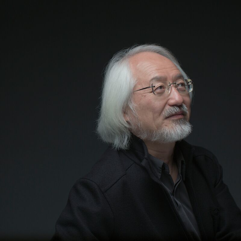 Head and shoulders portrait of conductor Masaaki Suzuki in a dark room