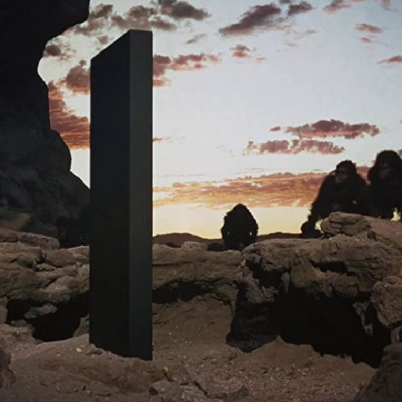 Film still from 2001: A Space Odyssey showing gorillas observing a monolith in a rocky landscape