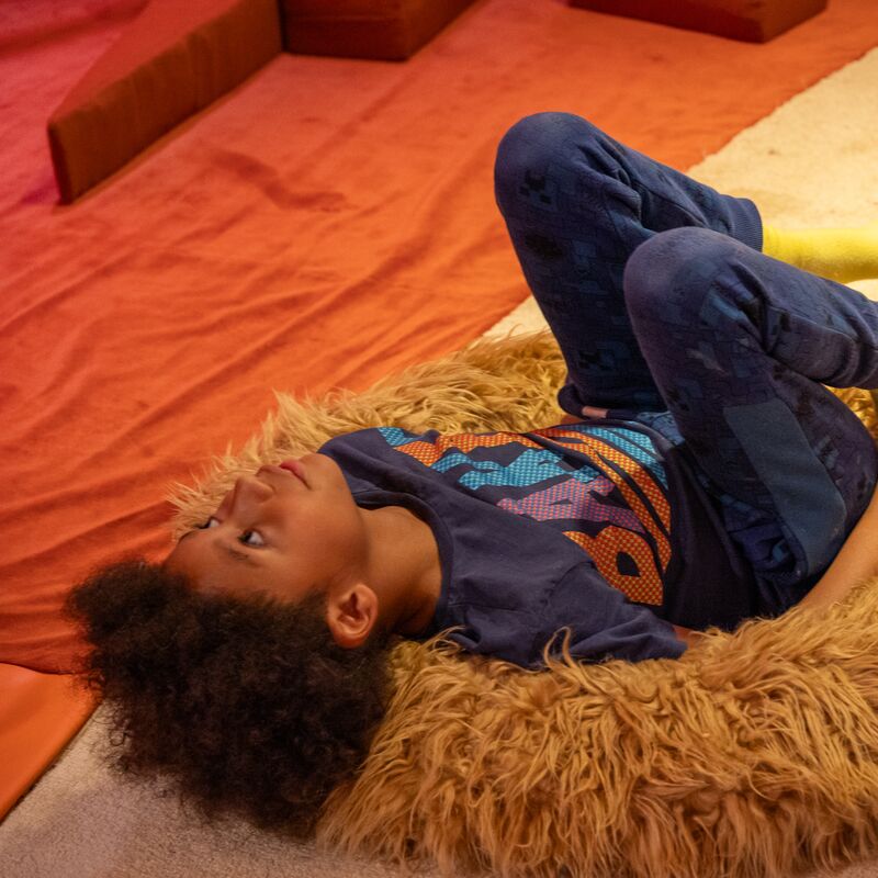 Child lying on their back on a fluffy yellow bean bag.