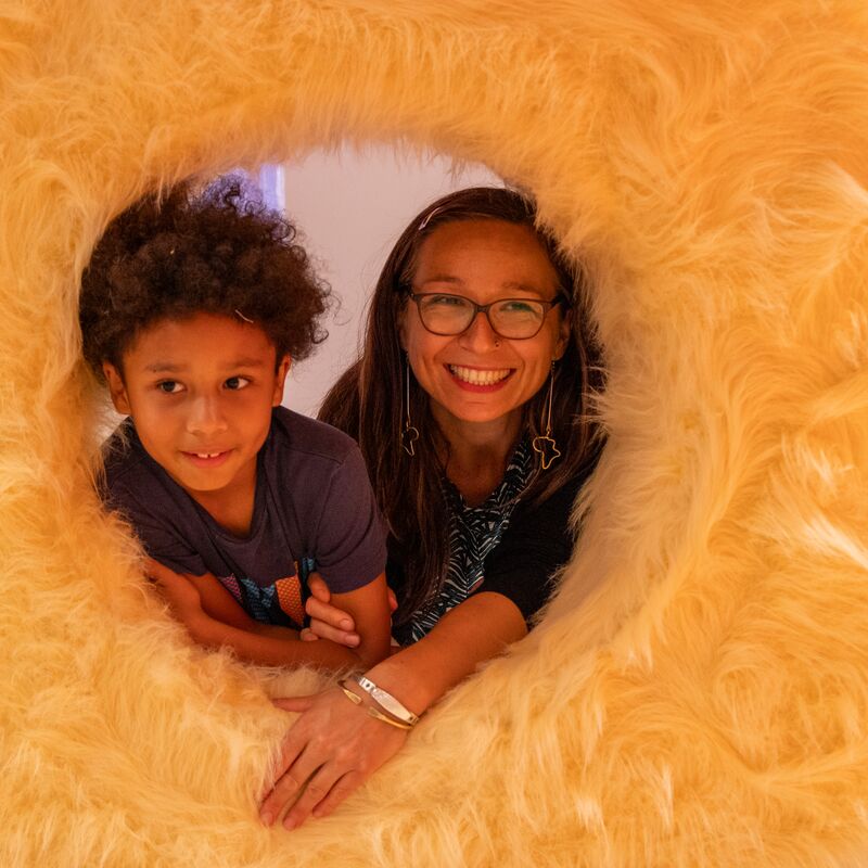 A woman and child look out of a hole inside a fluffy-looking object in REPLAY