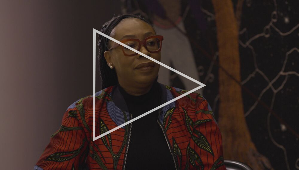 The artist Otobong Nkanga wearing red framed glasses and a multi-coloured jacket