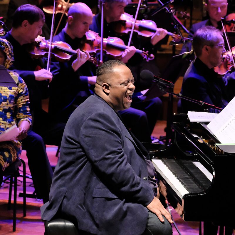 Pianist Julian Joseph performing live, seated in front of an orchestra