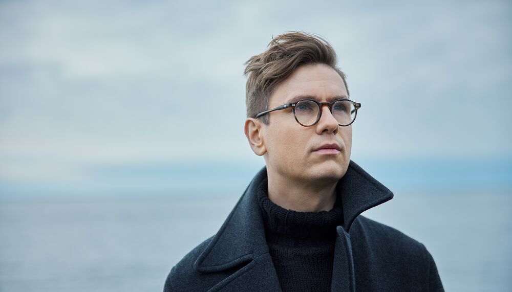A man wearing glasses and a black coat at the seaside.