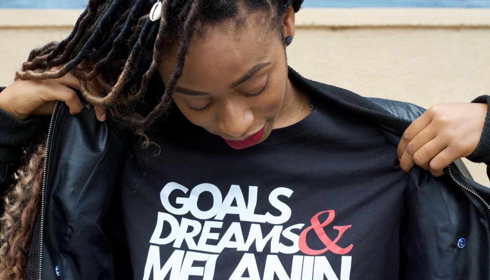 A girl is photographed wearing a t-shirt that says 'Goals, Dreams & Melanin'
