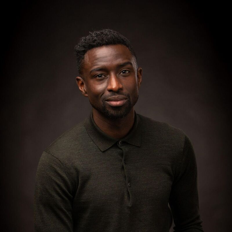 Jeffrey Boakye, a man wearing all black standing against a black background, clasping his hands
