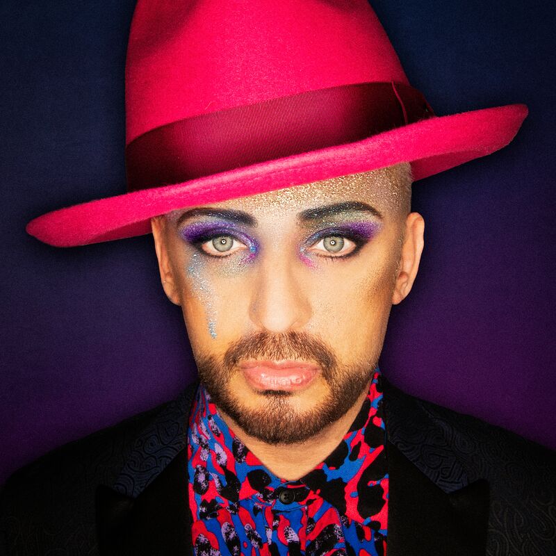 Boy George wears a pink and blue spotted jacket and a pink hat