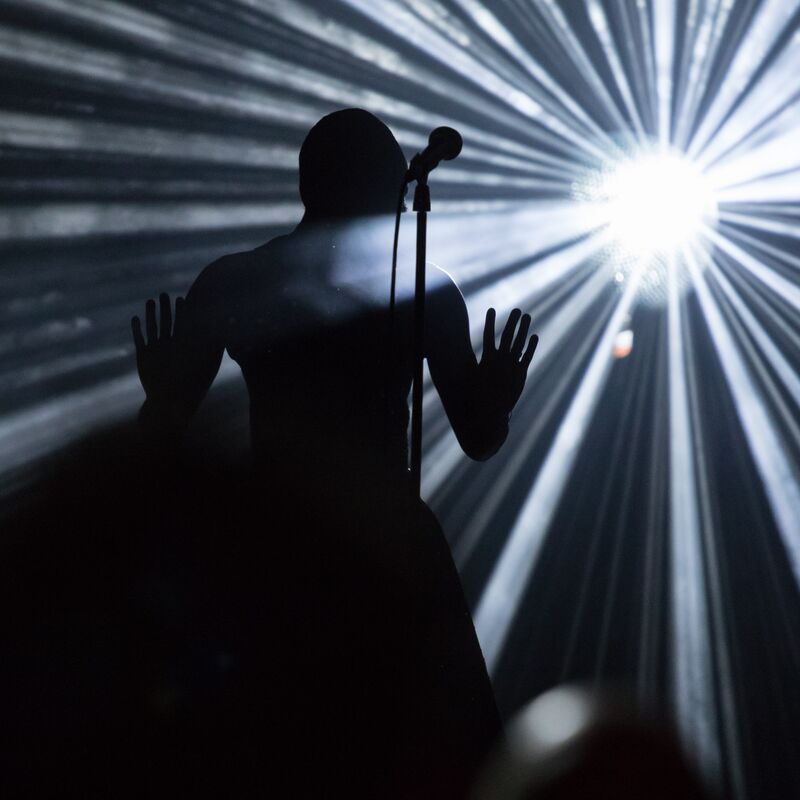 Silhouette of someone performing at a microphone eclipsed by a spotlight