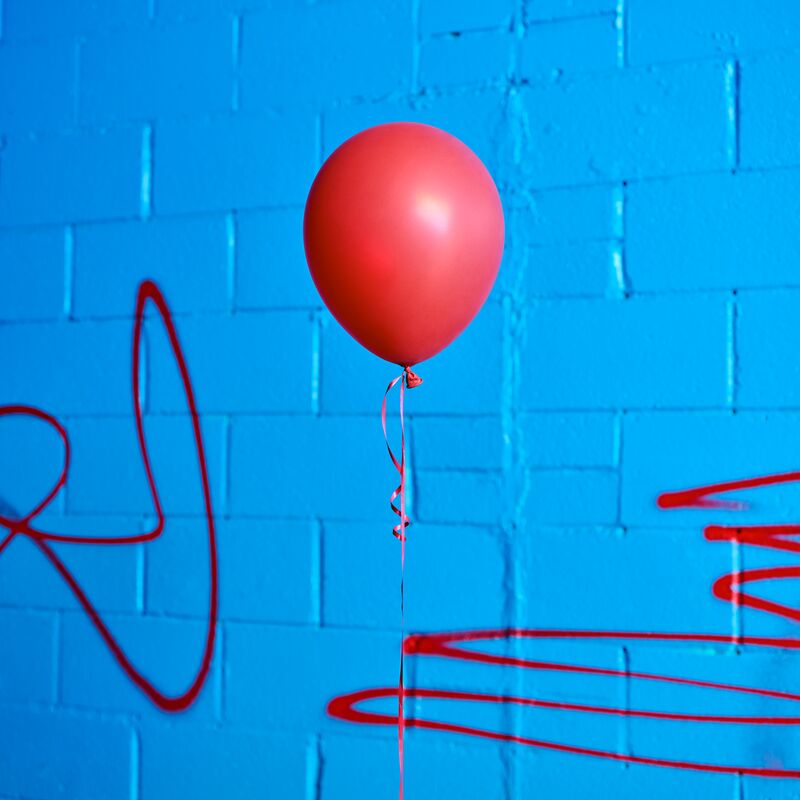 A red balloon against a bright blue wall with red graffiti