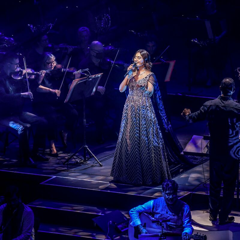 Person with a blue sparkly dress singing on stage with an orchestra
