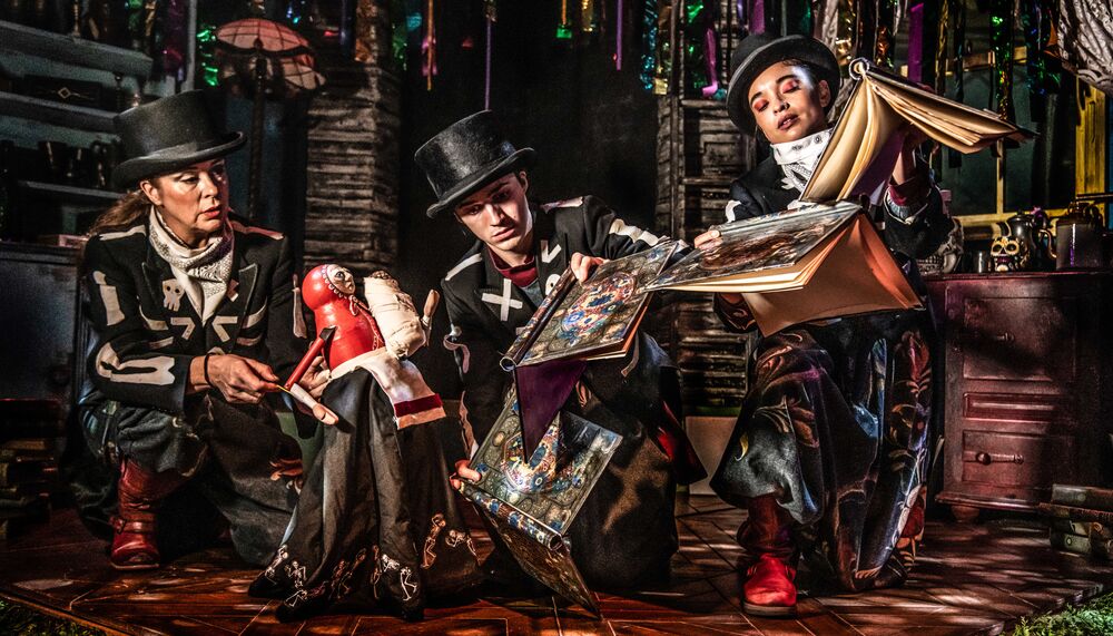 Three performers kneel holding books and puppets