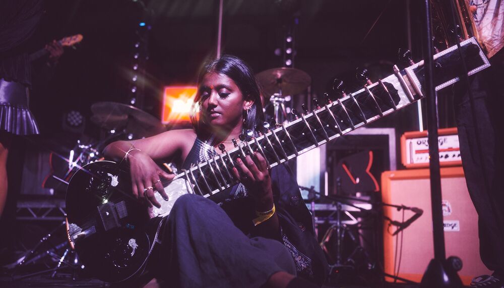 A seated person plays a shiny black sitar