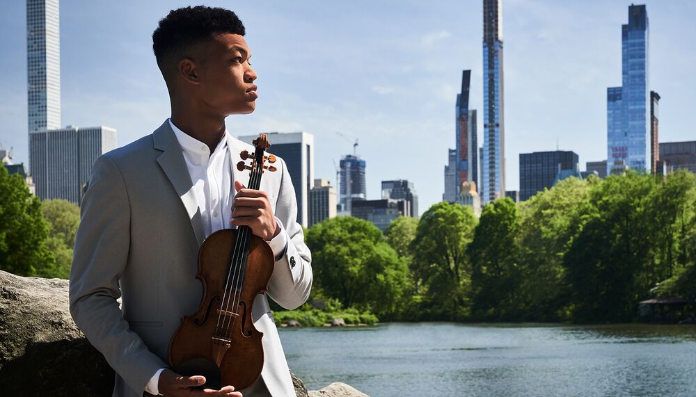 Randal Goosby holds a violin in the park looking off into the city