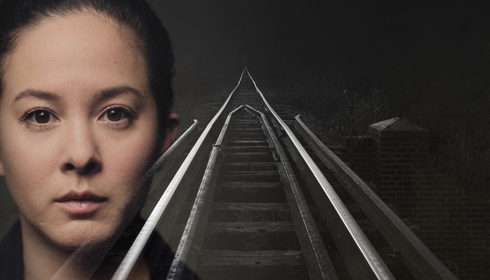 A double exposure of train tracks leading into the distance with a woman staring into the camera layered over it