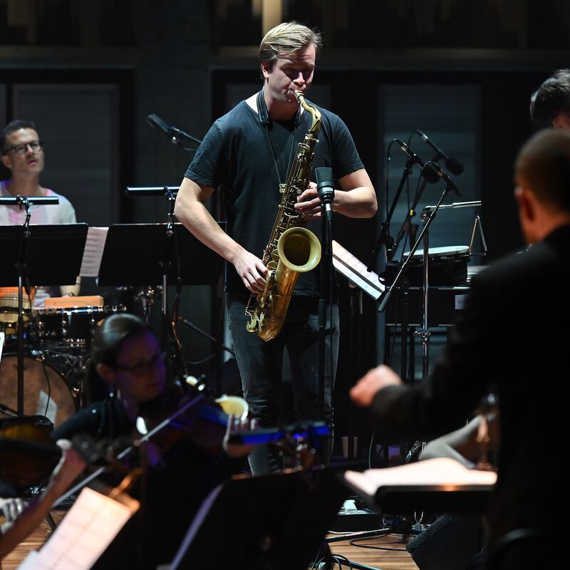 Marius Neset plays tenor sax in a recording studio surrounded by other musicians