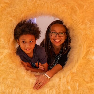 A woman and child poking their heads through a furry orange doughnut-shaped circle