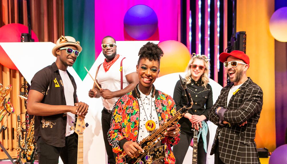 YolanDa Brown wearing a colourful jacket holding a saxophone surrounded by her band.