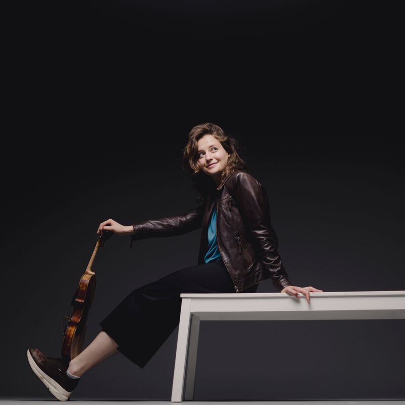Dana Zemtsov at on a white bench balancing a violin on her ankles