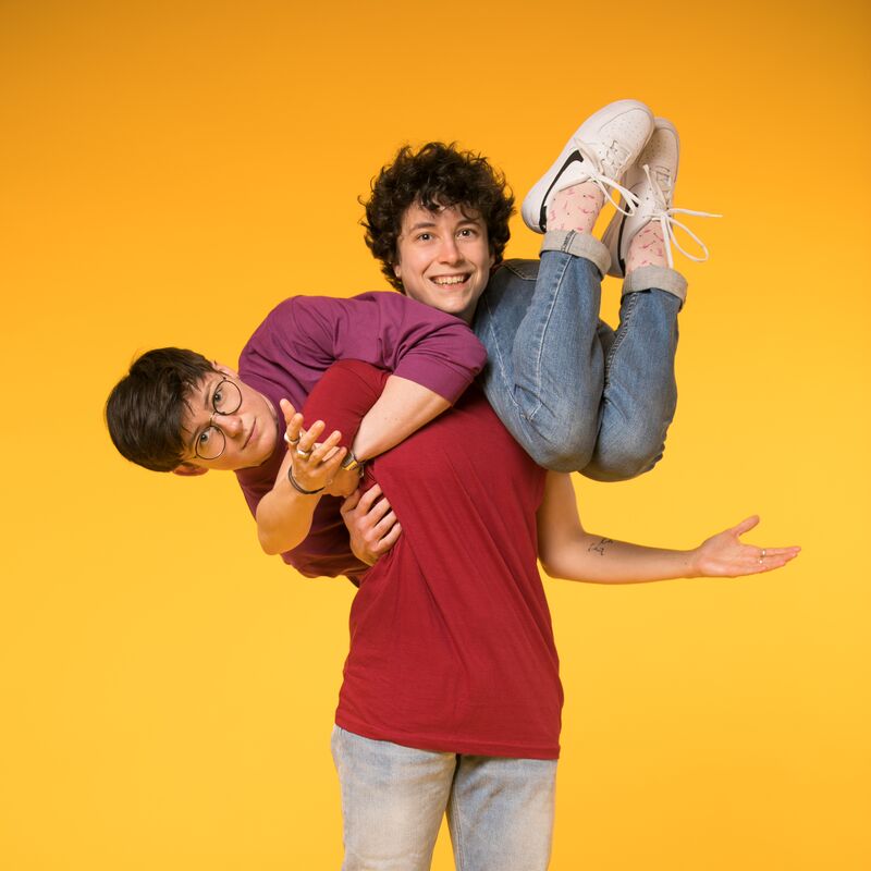 A person balancing on someone's shoulders against a yellow background