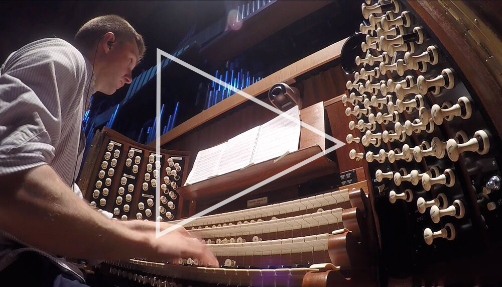 The Royal Festival Hall organ console, featuring a baffling number of white knobs; organist James McVinnie, a White man with a buzz cut is playing the organ keys