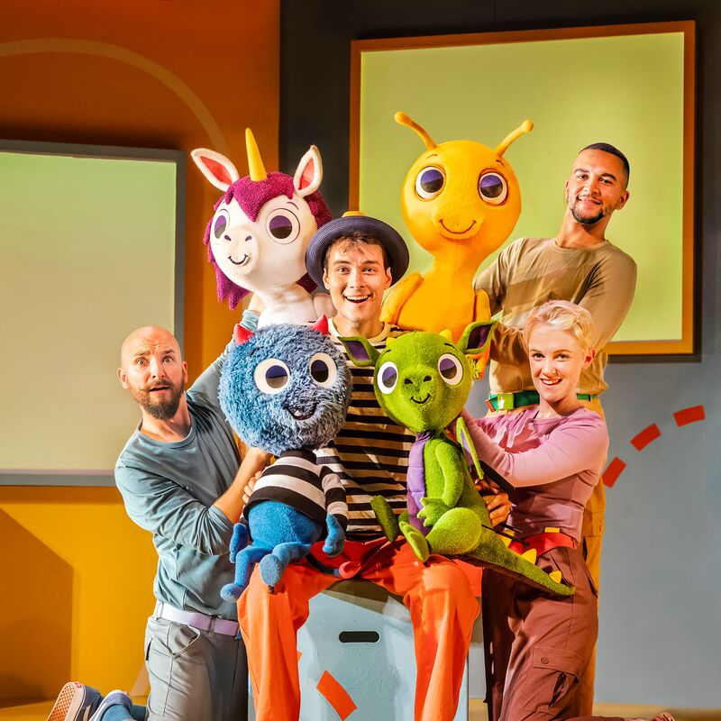 Four actors pose together holding colourful monster character puppets.