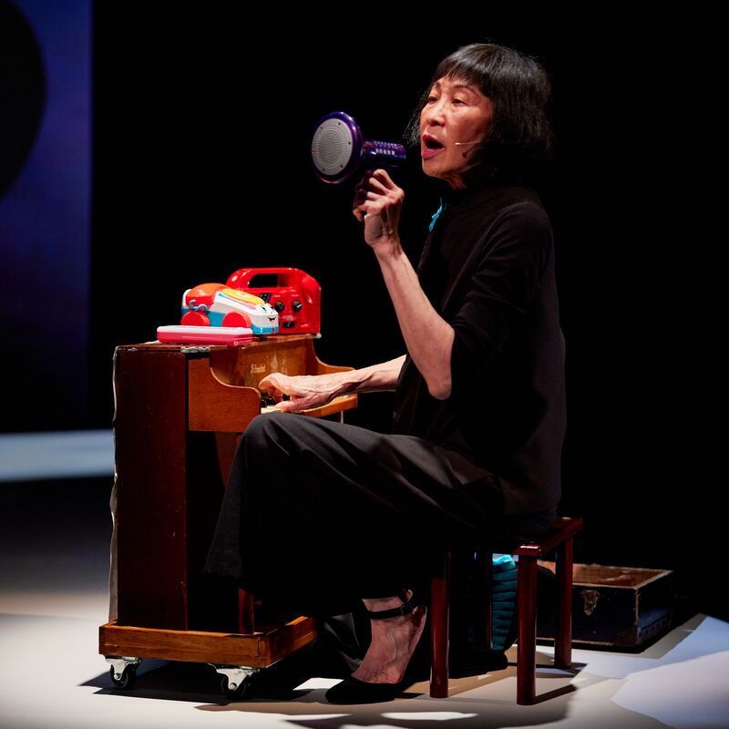 Margaret Leng Tan playing a toy piano and singing in a toy megaphone, on stage