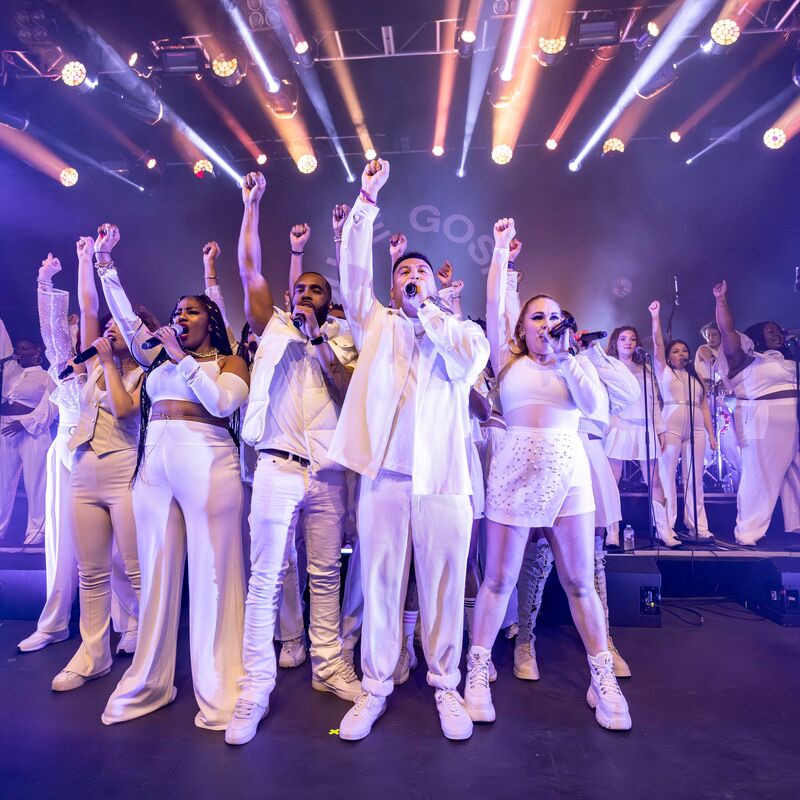 A choir dressed in all white posing with one arm raised