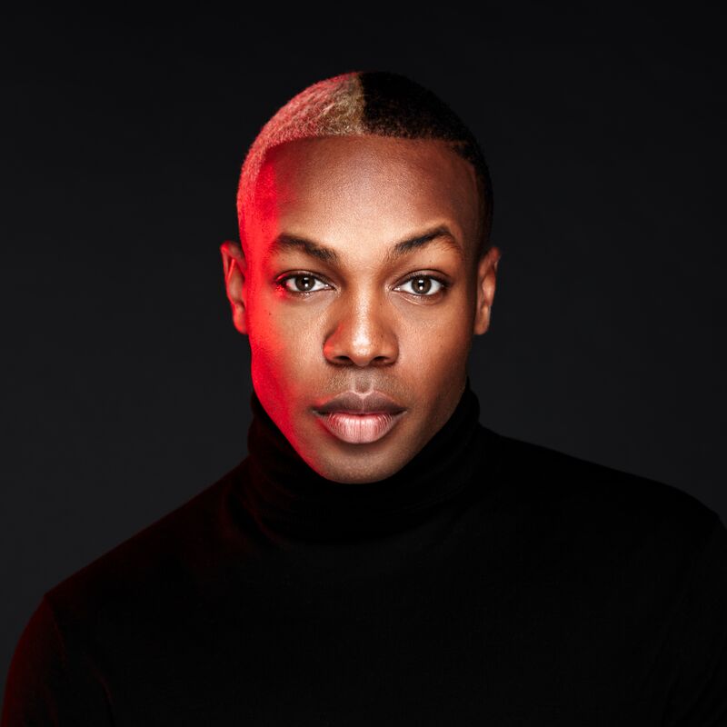 Todrick Hall staring directly into the camera, wearing a black turtle-neck shirt with half their hair blonde and half black.