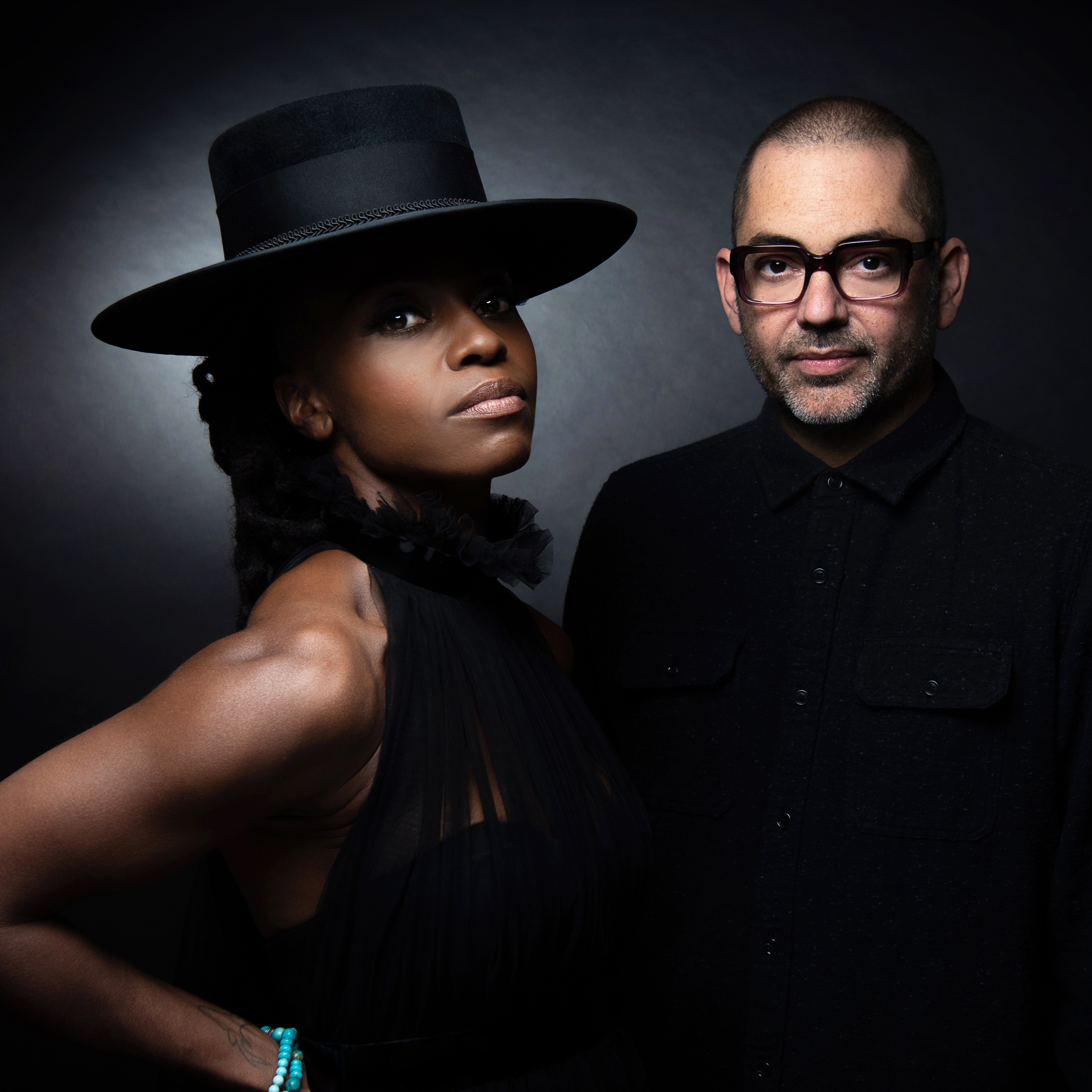 The Morcheeba duo wearing black pose against a black screen.