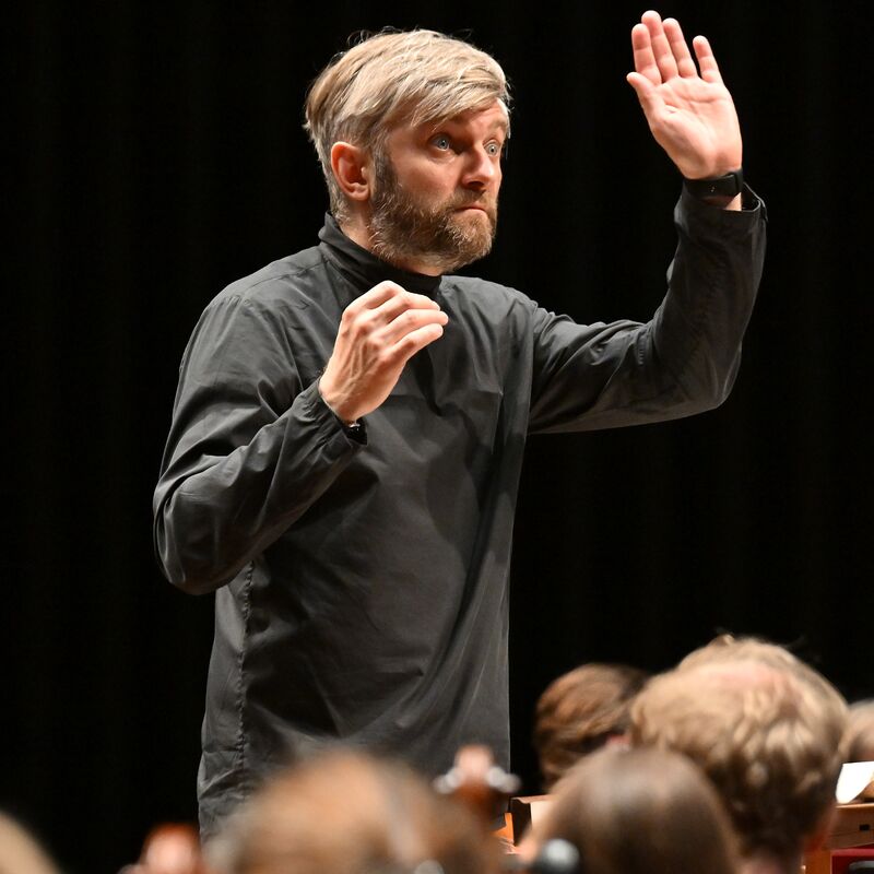 Conductor Kirill Karabits wearing a black outfit with this hand raised