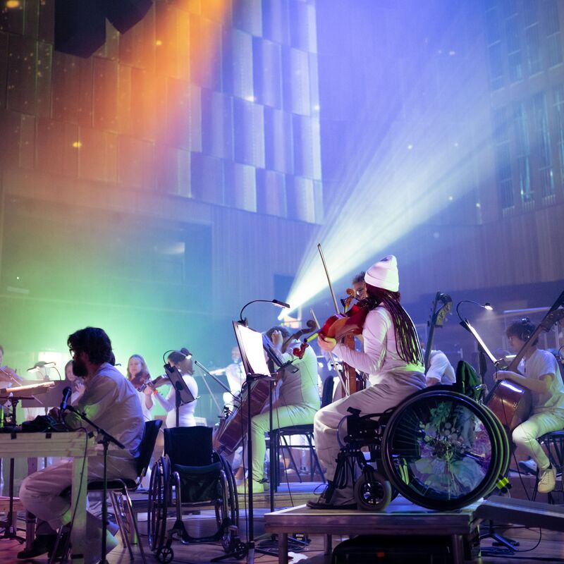Paraorchestra: Trip the Light Fantastic at the Bristol Beacon - the orchestra wear all white and are surrounded by colourful lights.