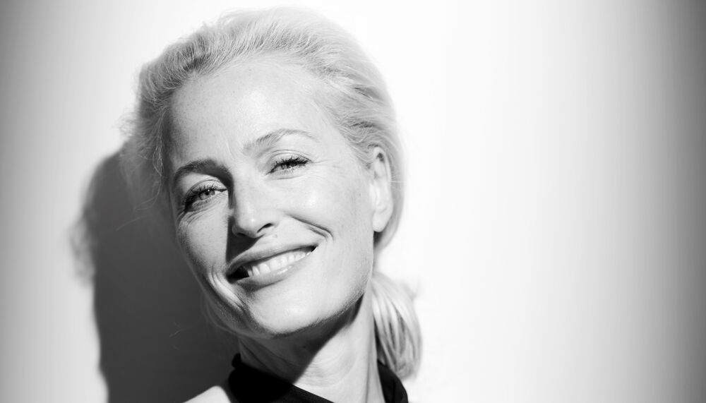 Gillian Anderson wears a black dress in a black and white photo