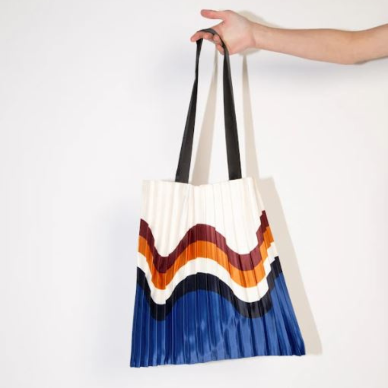 A pleated, colourful tote bag being held up by a hand belonging to someone outside the frame