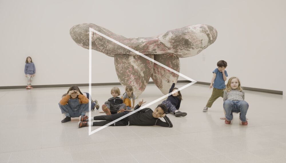 Several young children sit around a sculpture, part of the When Forms Come Alive exhibition, in the white space of the Hayward Gallery