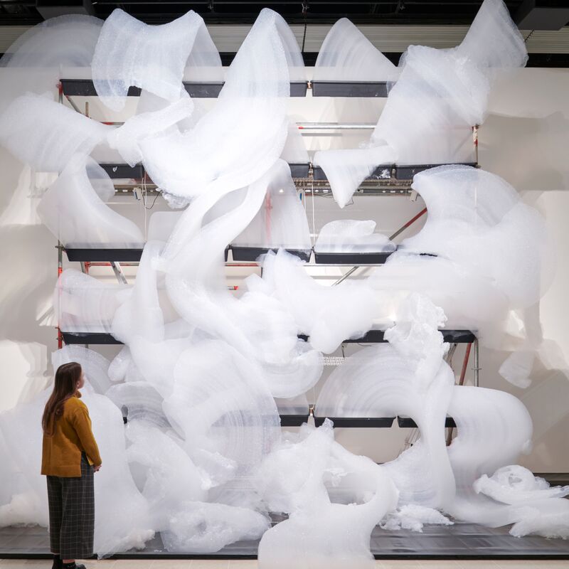 A person stands looking up at a bubbly sculpture
