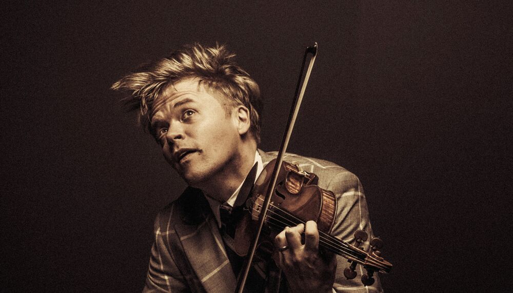 Violinist Pekka Kuusisto playing the violin. The picture has faded sepia tones and a dark background