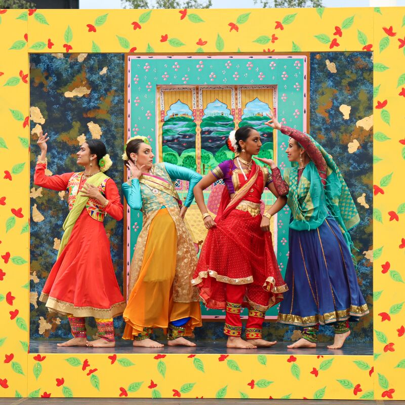 Four south asian women stand on a colourful stage wearing bright traditional clothing