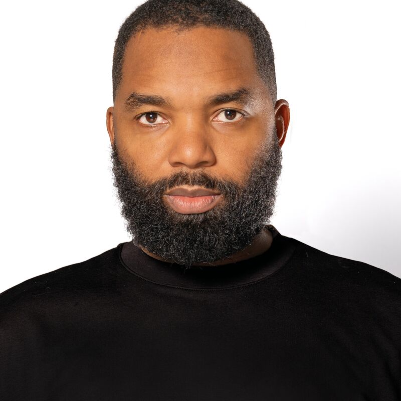 Tavares Strachan wearing a black tshirt standing in front of a white background.