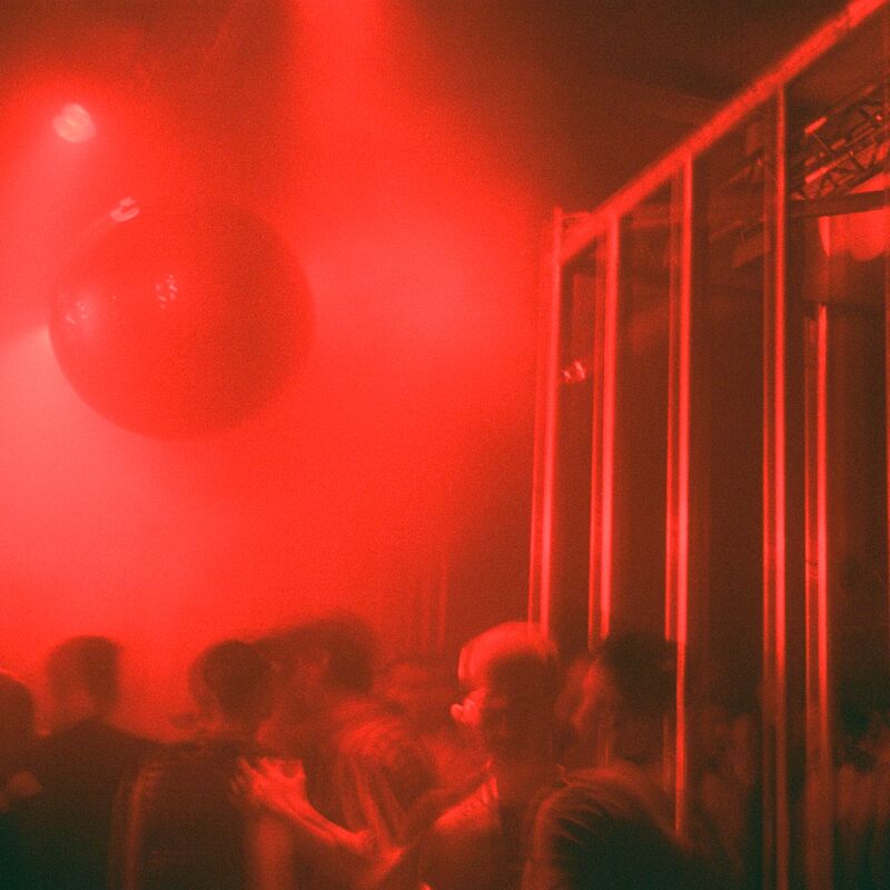 Hazy club scene of people dancing in moody red lighting.