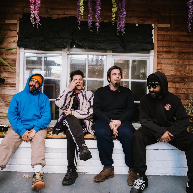 Members of the Speaker's Corner Quartet sitting on a low wall in front of a wooden house with plants around them.