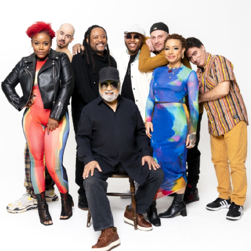 Members of Incognito standing and sitting together against a white background wearing different outfits.