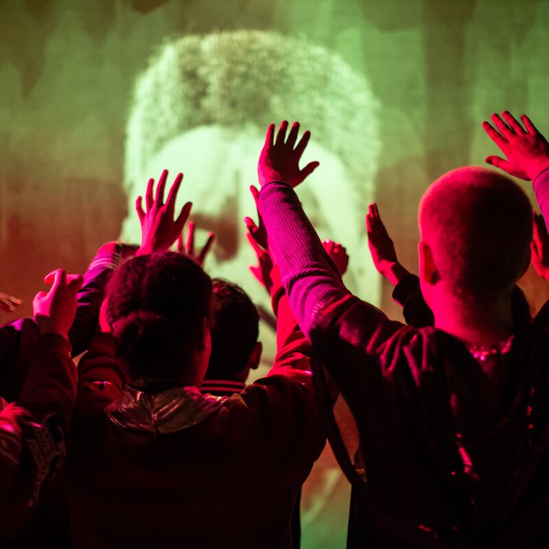 People lit in red hue, holding their hands up in front of projection