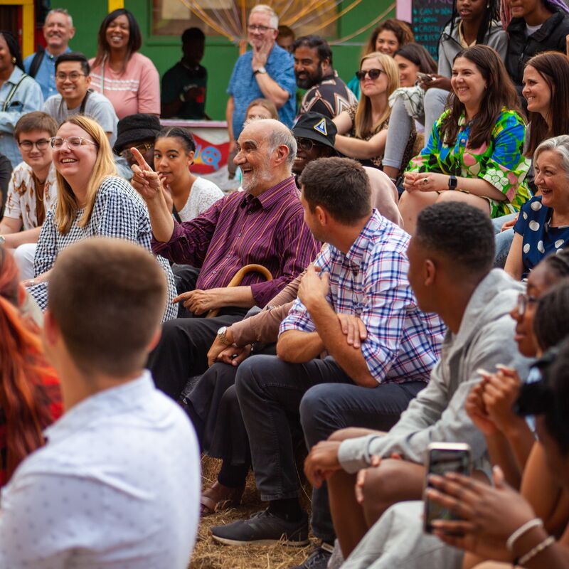 An audience sat on hay bales, staring at a man asking a question in the crowd