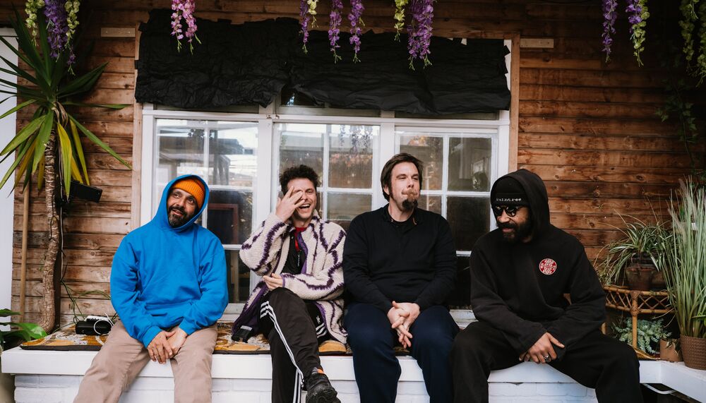 Members of the Speaker's Corner Quartet sitting on a low wall in front of a wooden house with plants around them.