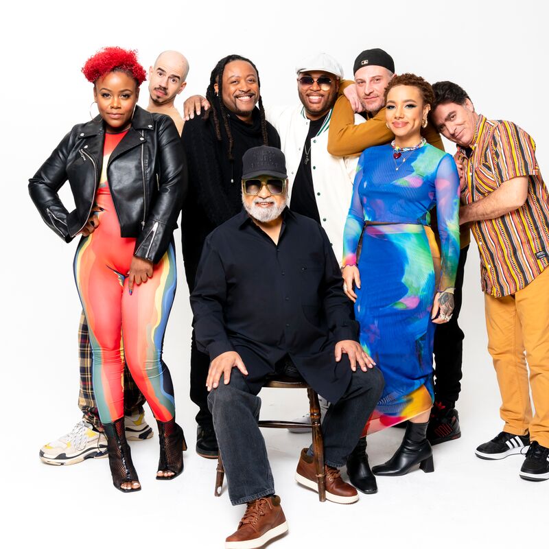 Members of Incognito standing and sitting together against a white background wearing different outfits.