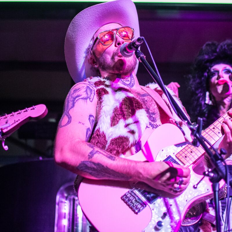 Members of Queer C*untry on stage, playing guitars