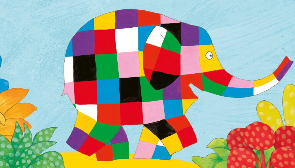 a large elephant covered in multicoloured square patches walks happily through flowers